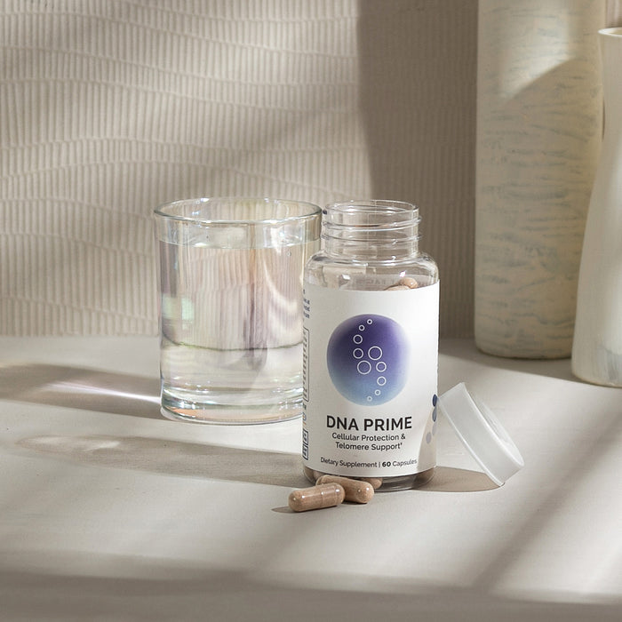 InfiniWell DNA PRIME dietary supplement bottle with capsules beside a glass of water, 60 capsules.