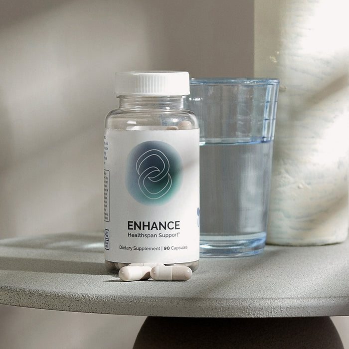 InfiniWell ENHANCE Healthspan Support supplement bottle beside a glass of water with capsules displayed, 90 capsules total.