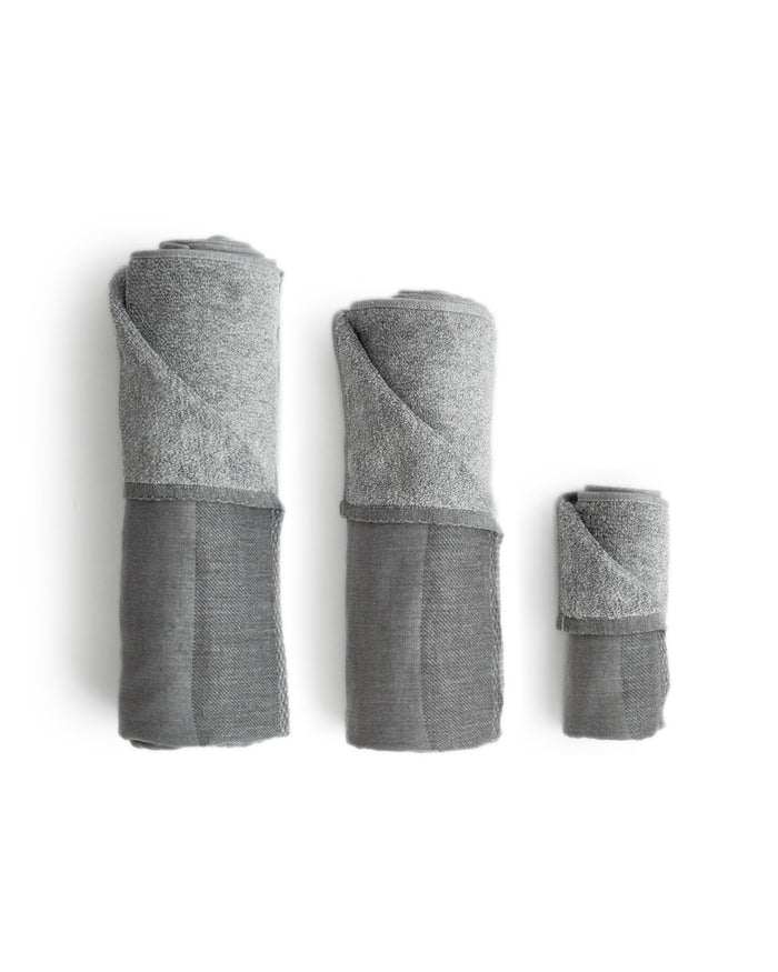 Silhouetted body, hand, and face zen charcoal towels rolled up placed next to each other, against white background.