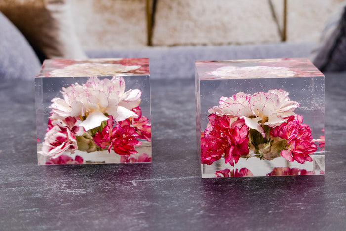 Two clear resin keepsake blocks preserving white and pink carnations from a wedding bouquet, displayed on a grey table.
