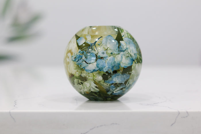 Landscape photo of a pressed flower candle sphere with dried botanicals on a styled surface