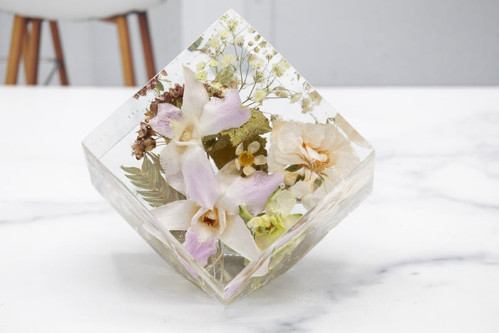 Resin geometric display with embedded orchid, greenery and accent flowers preserved flowers on a white surface