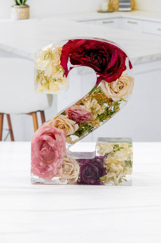 Floral number '2' made of preserved flowers on a white surface with a blurred background.