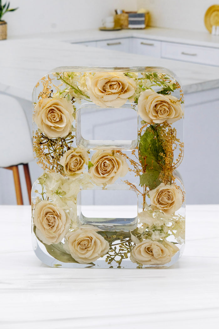 Resin Flower Preservation Number '8' made of preserved roses on a white surface with a blurred background.