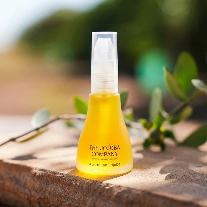 Bottle of The Jojoba Company Australian Jojoba oil on a stone surface with greenery in the background
