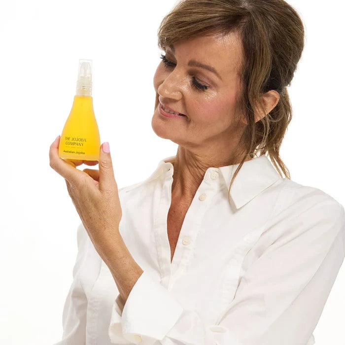 Woman holding a bottle of yellow jojoba oil against a white background