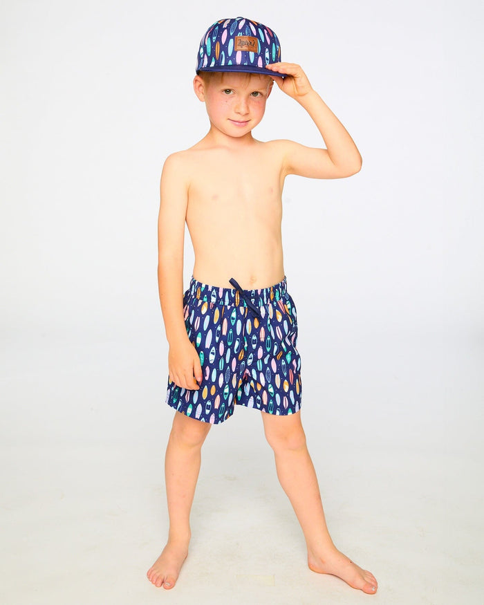 Boy standing in studio in navy surfboard swim shorts above the knee
