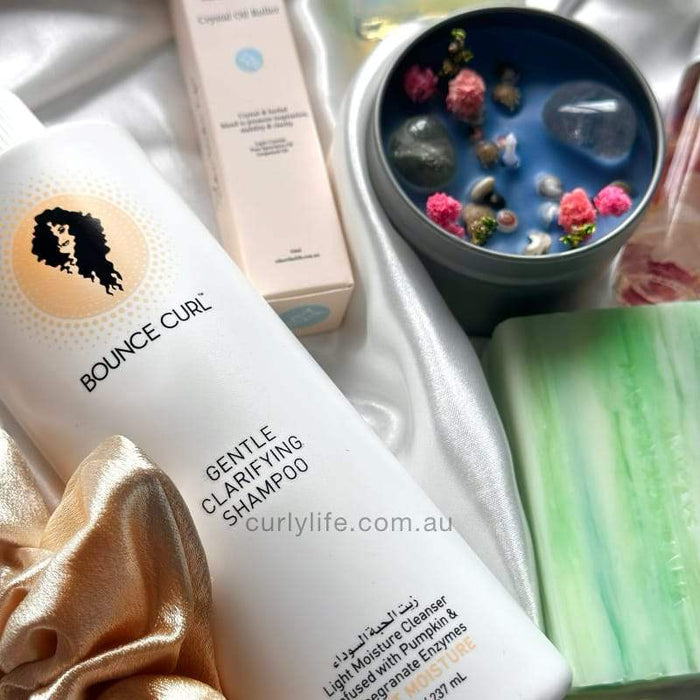 Bounce Curl Gentle Clarifying Shampoo with curly hair care essentials on satin fabric