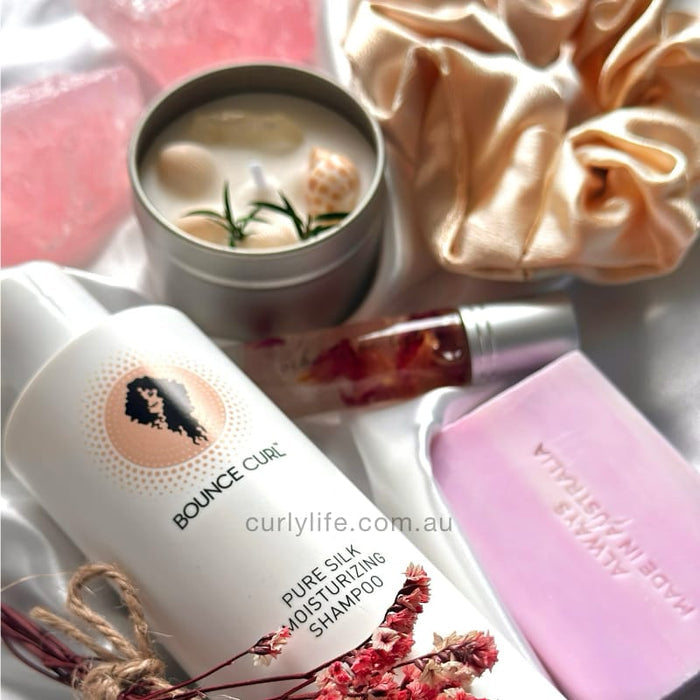 Bounce Curl Pure Silk Moisturizing Shampoo with silk scrunchie, pink soap, and decorative candle for curly hair care