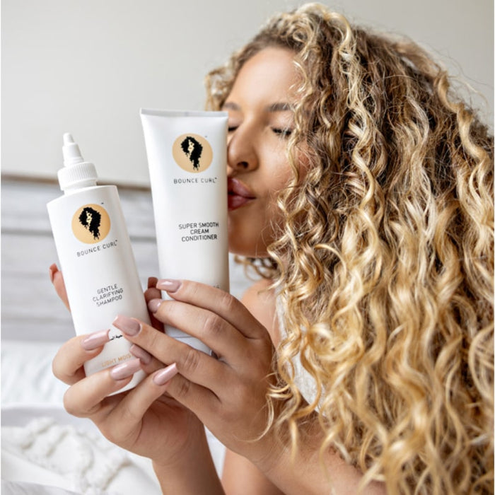 Woman with curly hair holding Bounce Curl Gentle Clarifying Shampoo and Super Smooth Cream Conditioner