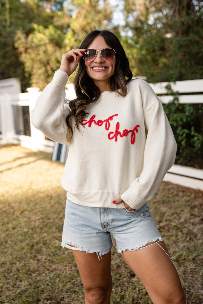 Woman wearing a white sweatshirt with red text and light blue shorts outdoors.