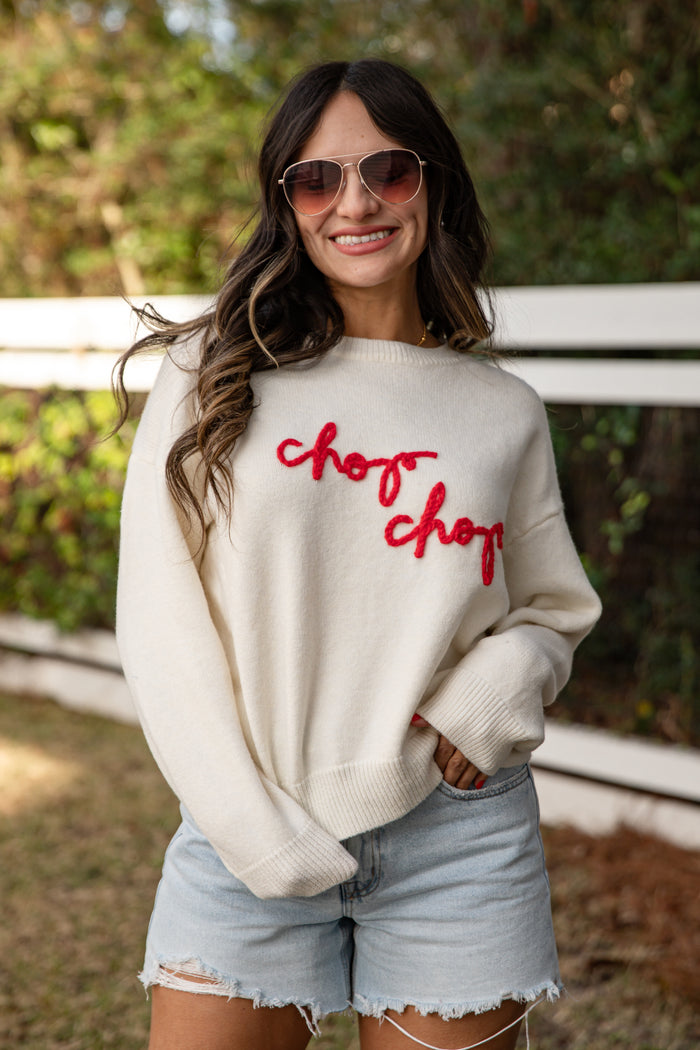 Woman wearing a white sweatshirt with 'chop chop' text, sunglasses, and denim shorts outdoors.
