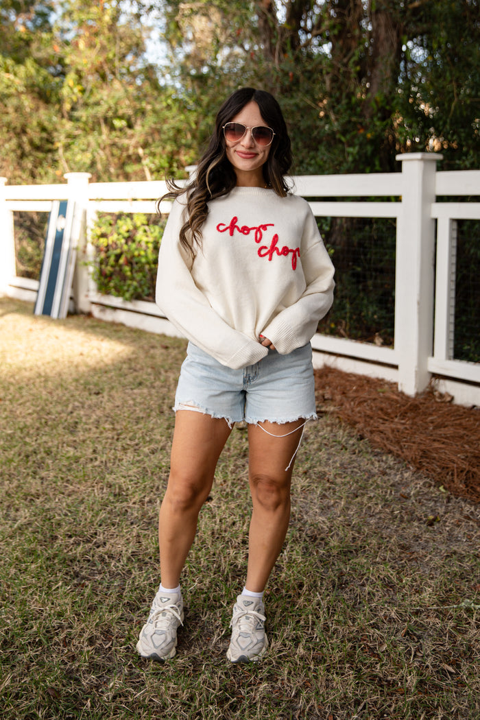 Woman wearing a white sweatshirt with red text and denim shorts outdoors.
