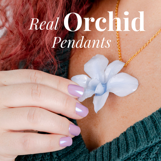 Real orchid pendants on a necklace worn by a person with pink nail polish.