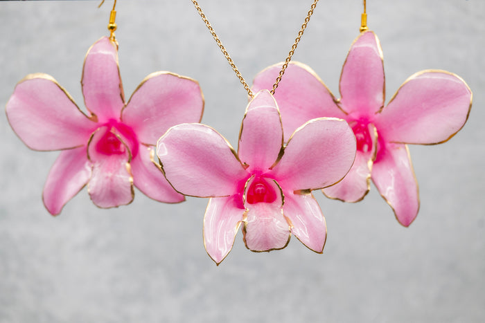 Pink orchid earrings with gold accents on a gray background