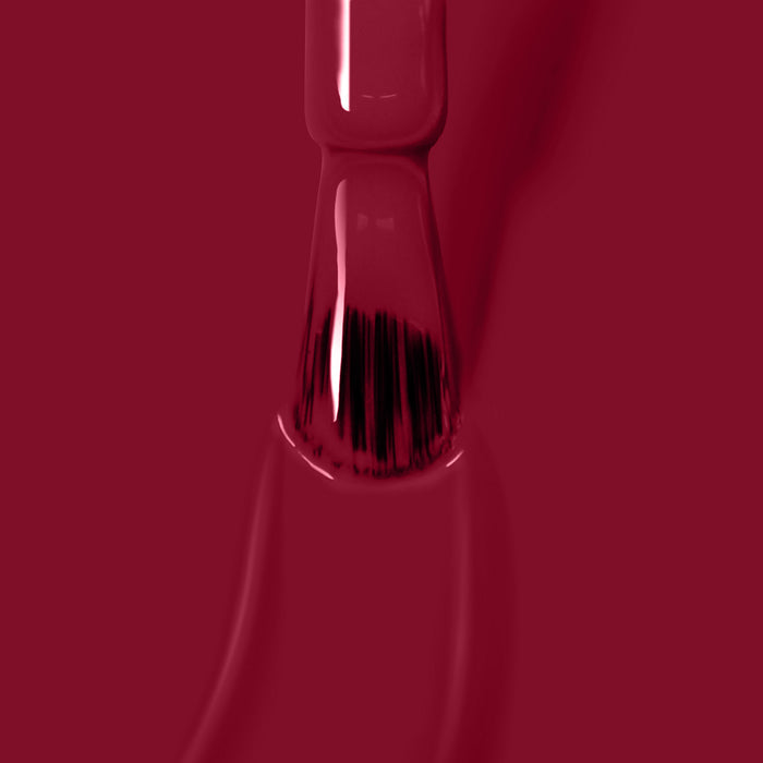 Close-up of a nail polish brush applying glossy Dragon Fruit, a vegan and cruelty-free nail polish by LONDONTOWN, on a surface.