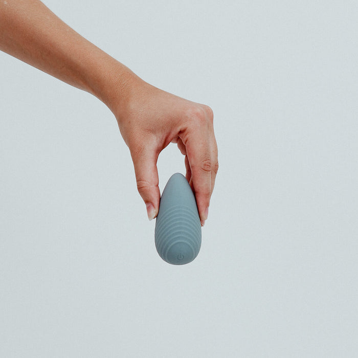 Hand holding Viola Green Eros Palm Vibrator in Stone colour, a small, palm-sized vibrator. Powerful vibrations, effortlessly controlled with a single button. Its grip-friendly design ensures a comfortable and pleasurable experience. Its discreet size also makes it the perfect travel buddy. It's crafted from sustainable materials, such as super silky body-safe silicone and is designed to combine sophistication with eco-consciousness, making it the perfect companion for sustainable pleasure seeker