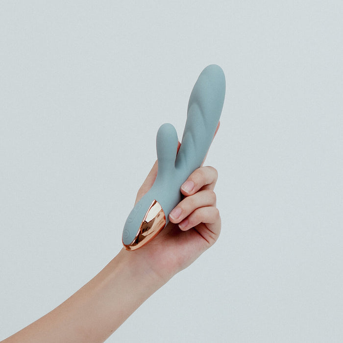 Hand holding Viola Green Essence Rabbit Vibrator in Periwinkle blue colour, a dual-action rabbit vibrator. With whisper-quiet motors and customisable settings, allowing you to tailor all your intimate experiences. Its ribbed shaft adds delightful textures, taking your pleasure to elevated heights. Crafted from sustainable materials, Essence is an eco-friendly choice that combines sophistication with responsible pleasure, ensuring every intimate moment is both satisfying and guilt-free.