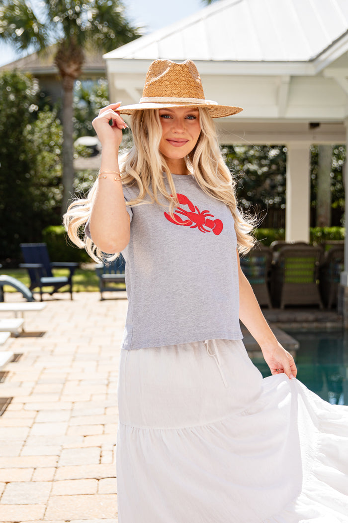 Woman wearing a gray t-shirt with a red lobster design and a white skirt by a pool.