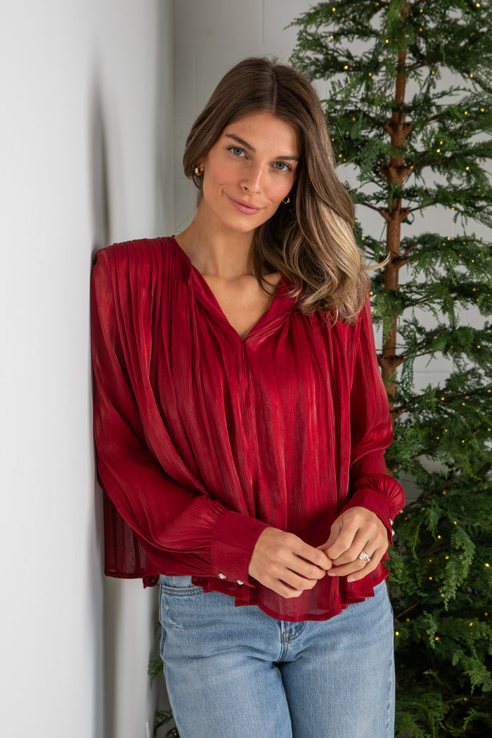Woman wearing a red blouse and blue jeans standing next to a Christmas tree.