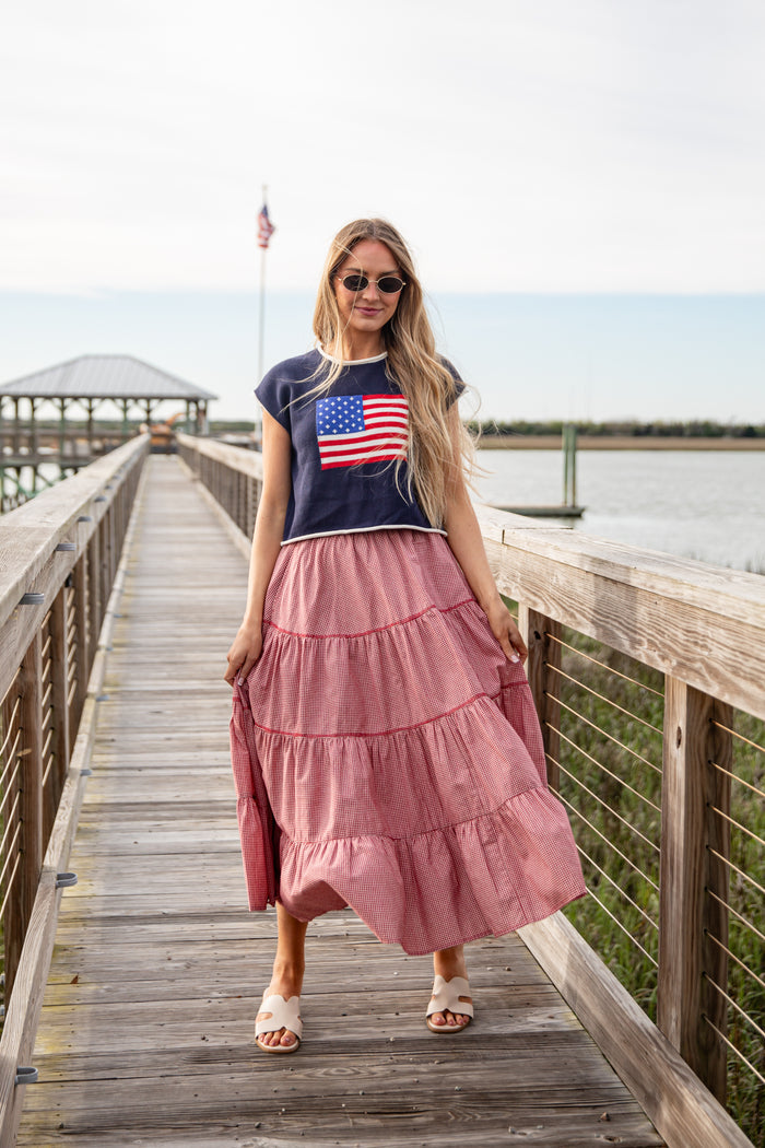 Woman wearing a navy t-shirt with an American flag design and a pink skirt on a wooden dock.