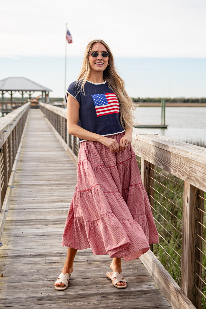 Woman wearing a navy t-shirt with an American flag and a pink skirt on a wooden dock.