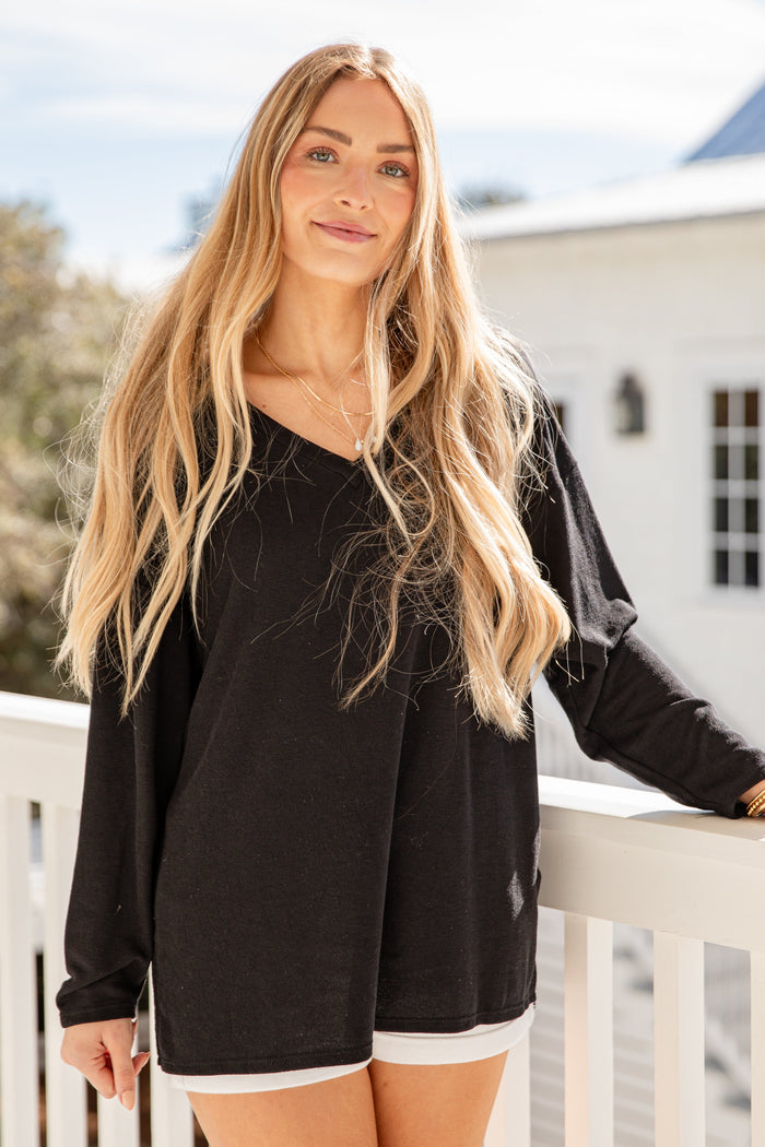 Woman wearing a black long-sleeve top and white shorts on a balcony.