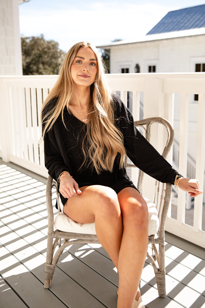 Woman sitting on a chair on a wooden deck with a white railing and building in the background.