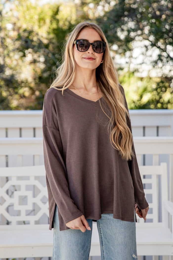 Woman wearing a brown long-sleeve top and sunglasses outdoors.