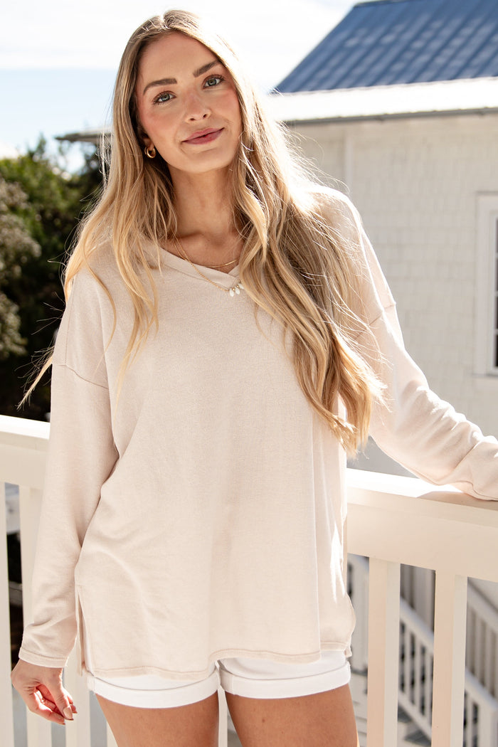 Woman in a beige sweater and white shorts standing on a balcony.