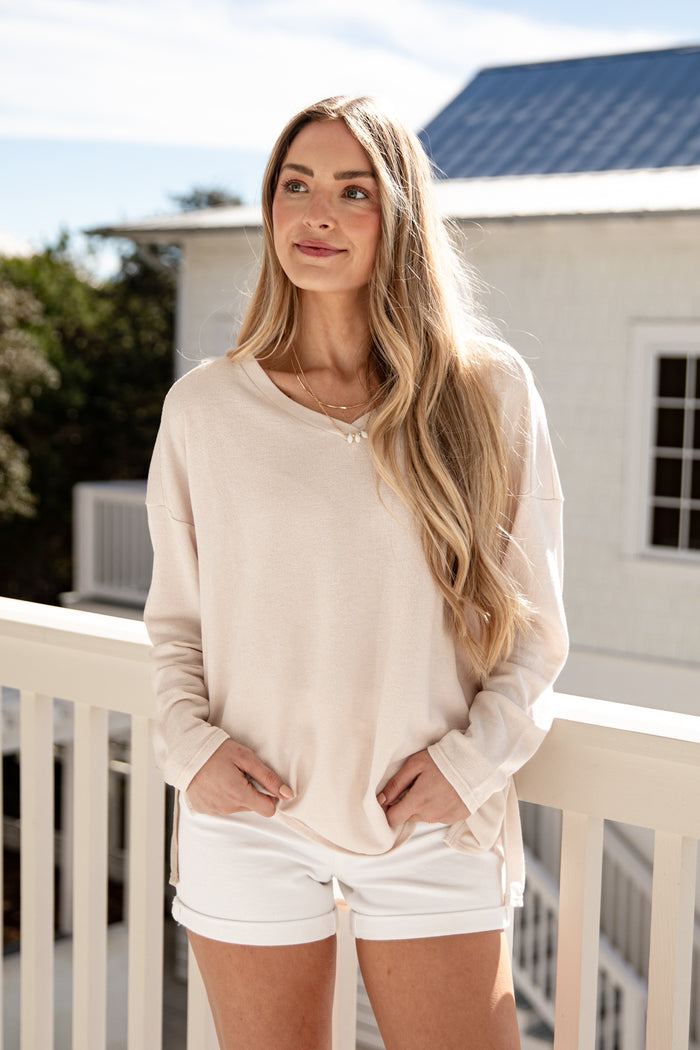 Woman wearing a beige long-sleeve shirt and white shorts on a balcony.