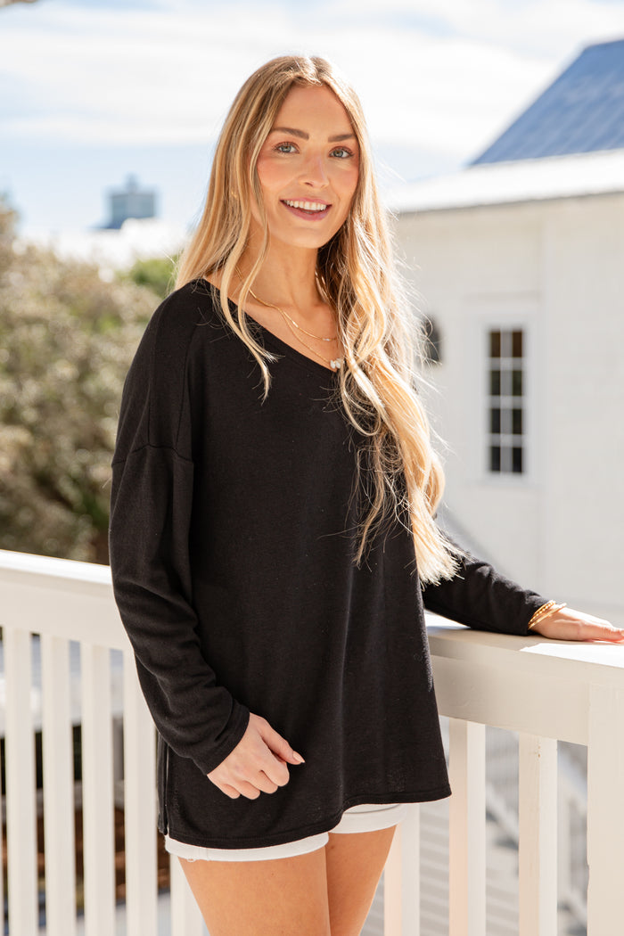 Woman wearing a black long-sleeve top and white shorts standing on a balcony.