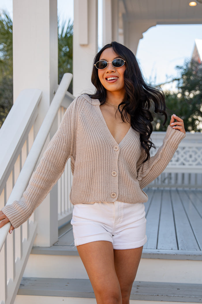 Woman wearing a beige cardigan and white shorts standing on a porch.