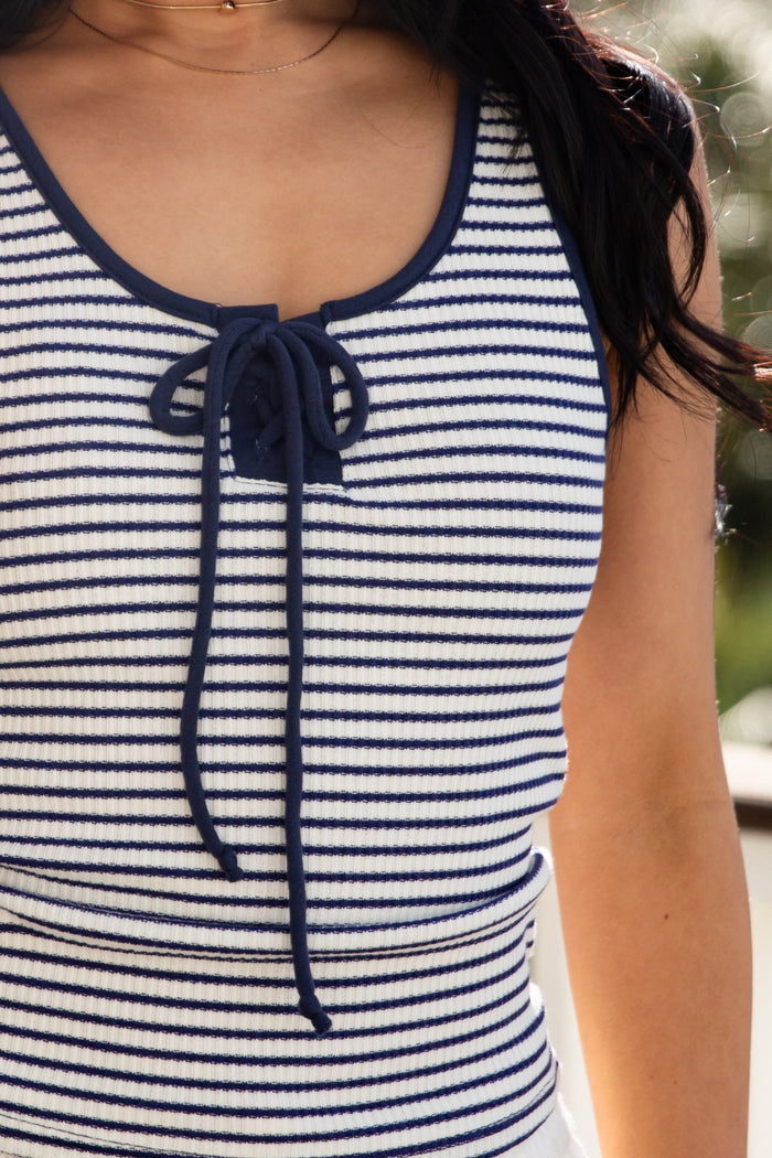 Close-up of a person wearing a blue and white striped tank top with a blurred background.