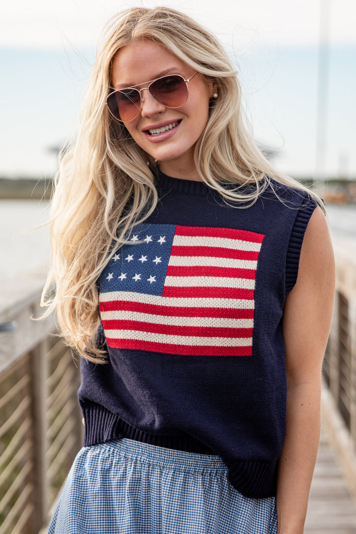 Woman wearing a sleeveless sweater with an American flag design on a wooden bridge.
