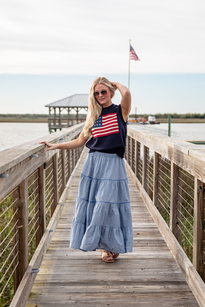 Woman standing on a wooden boardwalk wearing an American flag shirt and blue skirt.