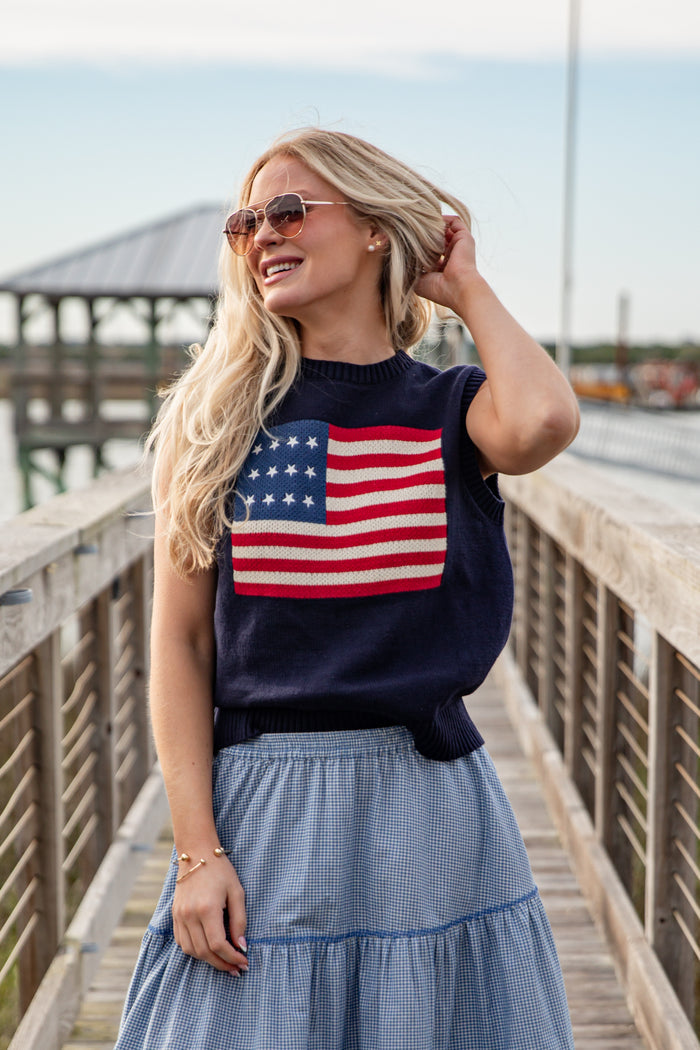 Woman wearing a navy sweater with an American flag design on a wooden pier.