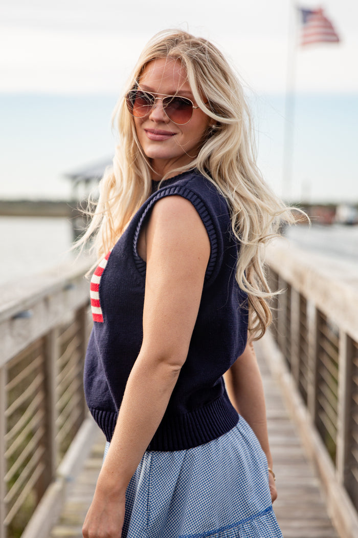 Woman wearing a navy sleeveless sweater and sunglasses on a wooden pier.
