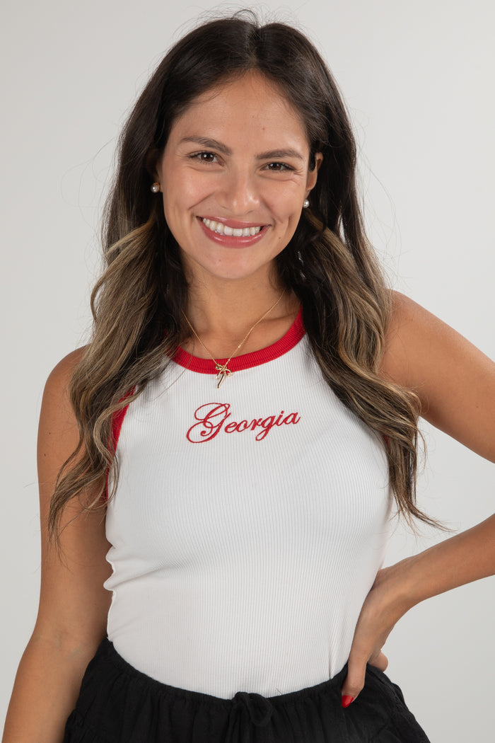 Woman wearing a white tank top with red trim and 'Georgia' printed on it, against a plain background.