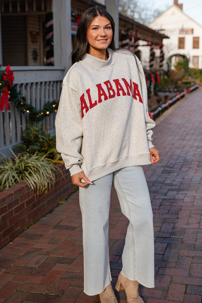 Woman wearing a 'Alabama' sweatshirt on a brick sidewalk with a building in the background