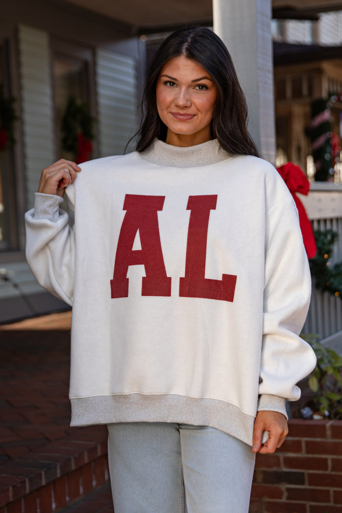 Woman wearing a white sweater with 'AL' in red letters, standing outdoors.