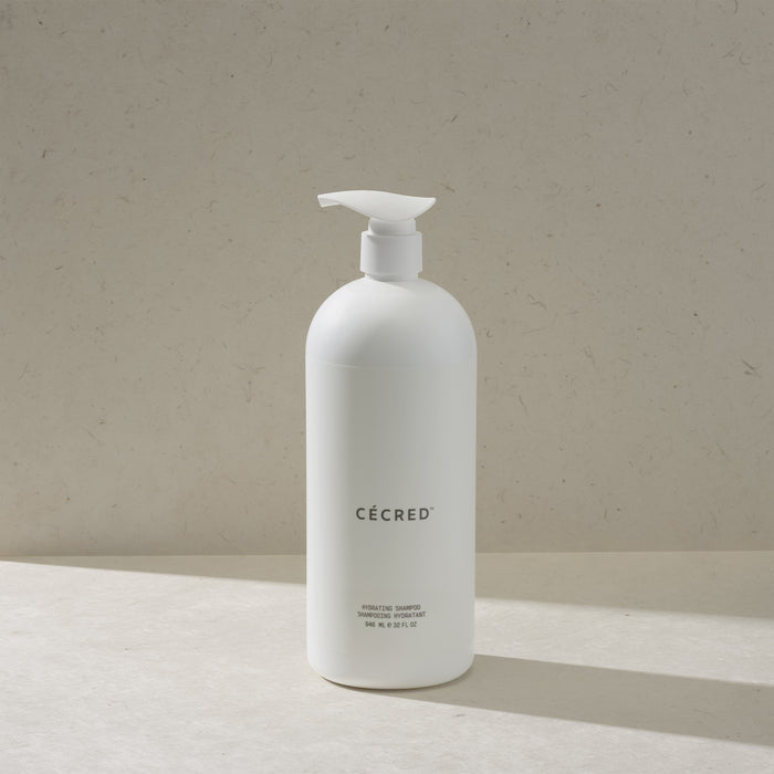 Cécred Hydrating Shampoo in the max size pump bottle, standing on a beige surface against a tan textured background