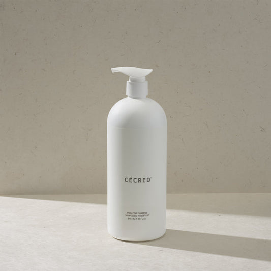 Cécred Hydrating Shampoo in the max size pump bottle, standing on a beige surface against a tan textured background