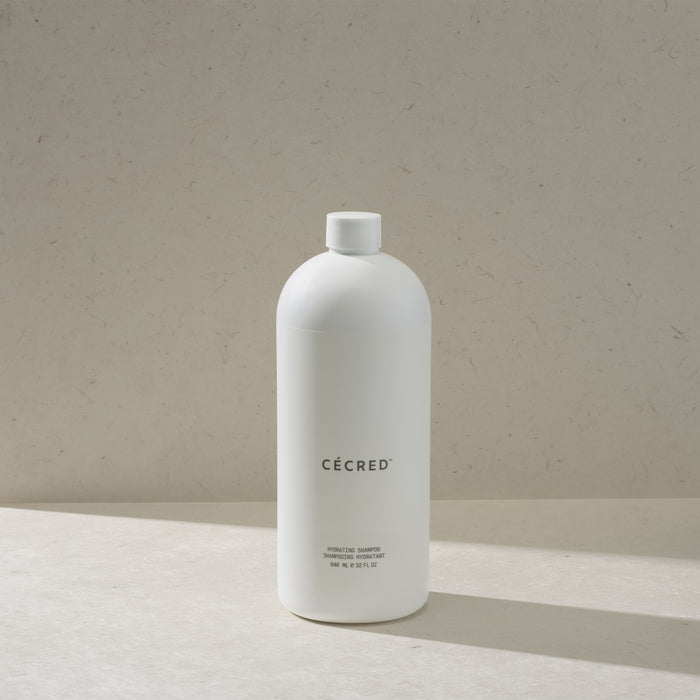 Cécred Hydrating Shampoo max size bottle with flip cap, standing on a beige surface against a tan textured background