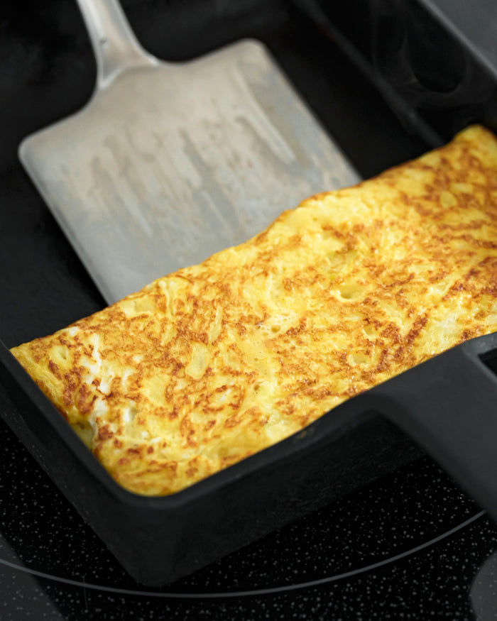 Close up cooked omelette in a cast iron pan with a spatula scooping the egg