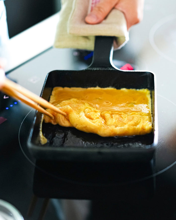 Person flipping a omelette in a cast iron pan on a stove