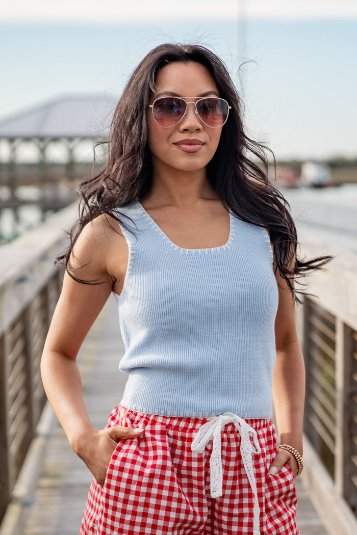 Woman wearing a light blue sleeveless top and red checkered shorts on a wooden bridge.
