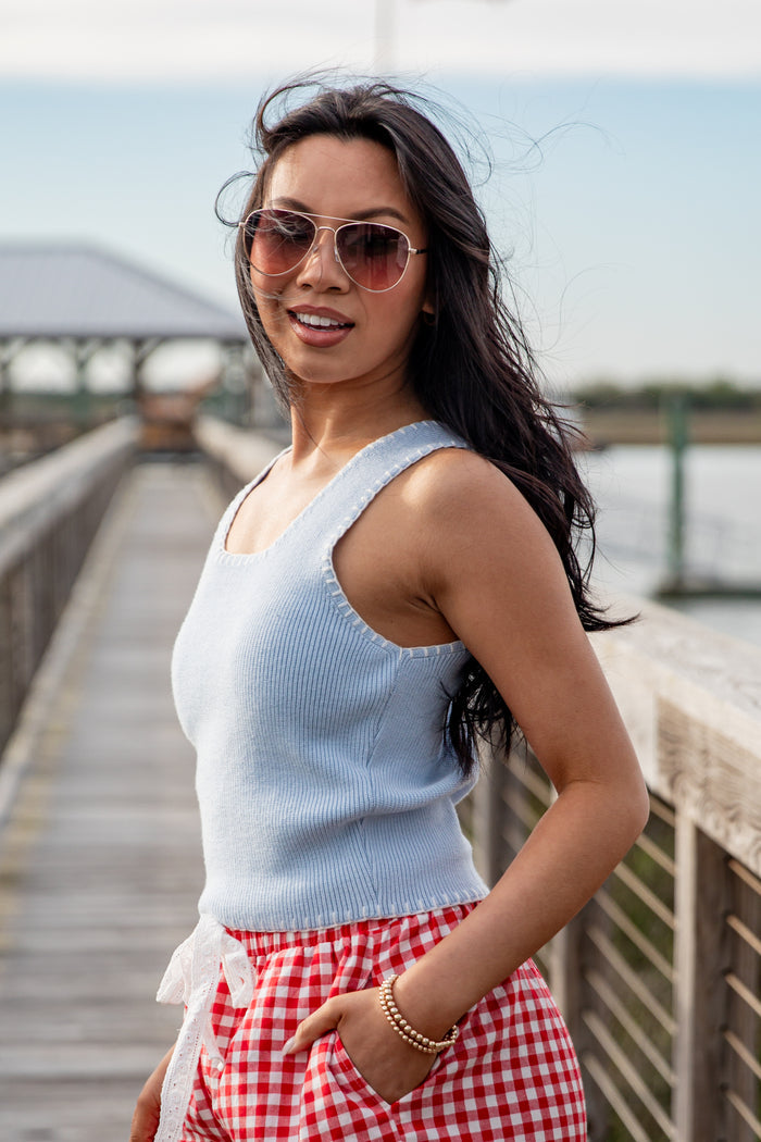 Woman wearing a light blue sleeveless top and red checkered shorts on a wooden pier.