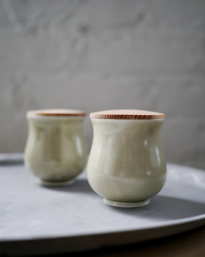 Two celadon lidded teacups are placed on top of a stainless steel tray.