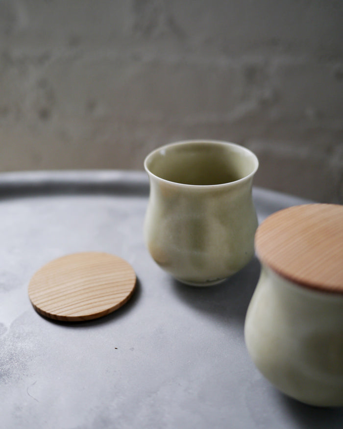Two celadon lidded teacups are placed on top of a stainless steel tray. The wood lid on one of the lidded teacup is off and set aside.